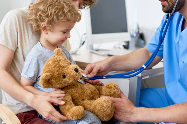 A young child holds a stuffed animal while a medial professional shows him how the stethoscope works. 