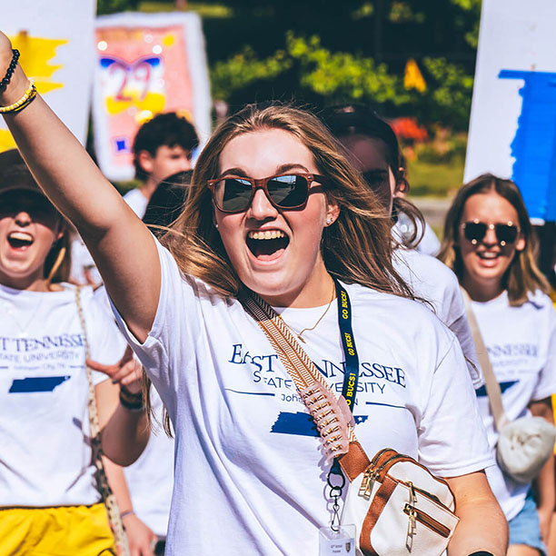 ETSU students smiling for the camera and waving during a campus event