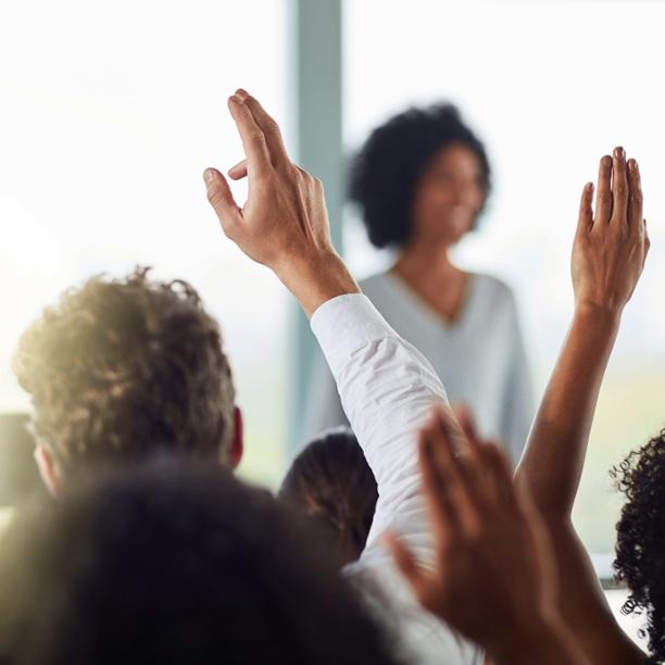 Person speaking to a group of people with their hands raised in question