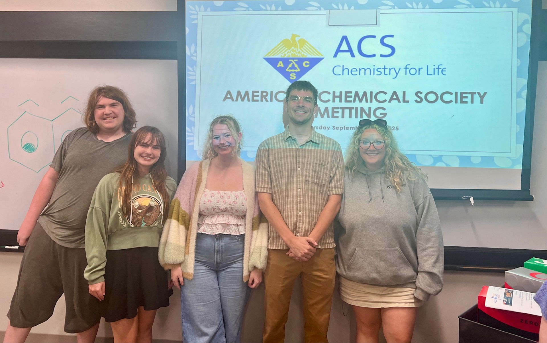 Five students standing before a projector with a ACS powerpoint on it.