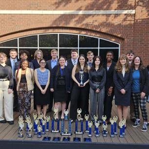 Speech and debate students standing behind a line of trophies
