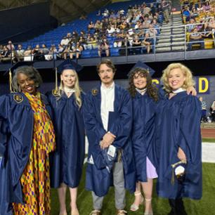 Five students dressed in graduation cap and gown smiling at the camera