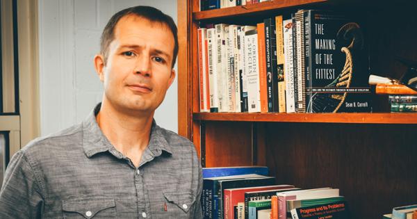 Dr. David Harker posing in front of a row of bookshelves