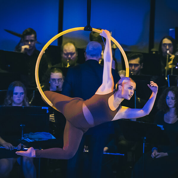 Aerialist in a hoop on a stage among a group of musicians playing a concert