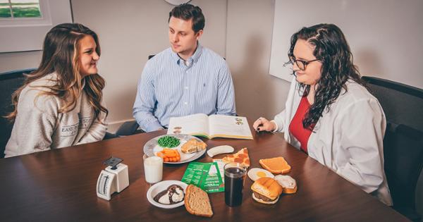 An ETSU nutritionist consults with patients on best nutrition practices. They sit at a table together and on the table are various fake foods to represent food groups.