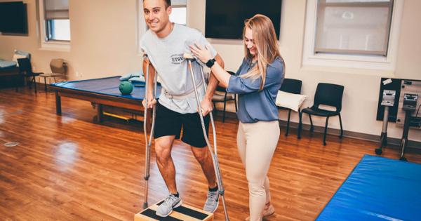 ETSU students practicing physical therapy techniques. One student is walking on crutches while the other supports them while walking.