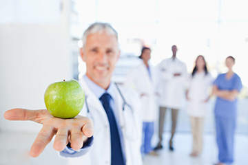 Physician holding apple in front of healthcare team