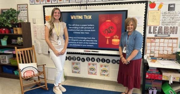 Two women standing infront of classroom board. 