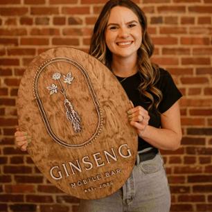 Tara smiling holding a Ginseng mobile bar sign
