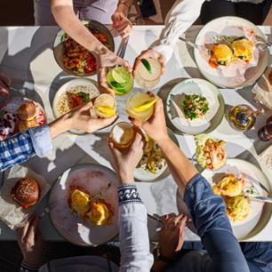 Friends eating and cheering drinks around the table.