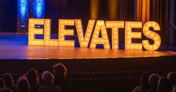 Lit up sign on stage that says "Elevates"