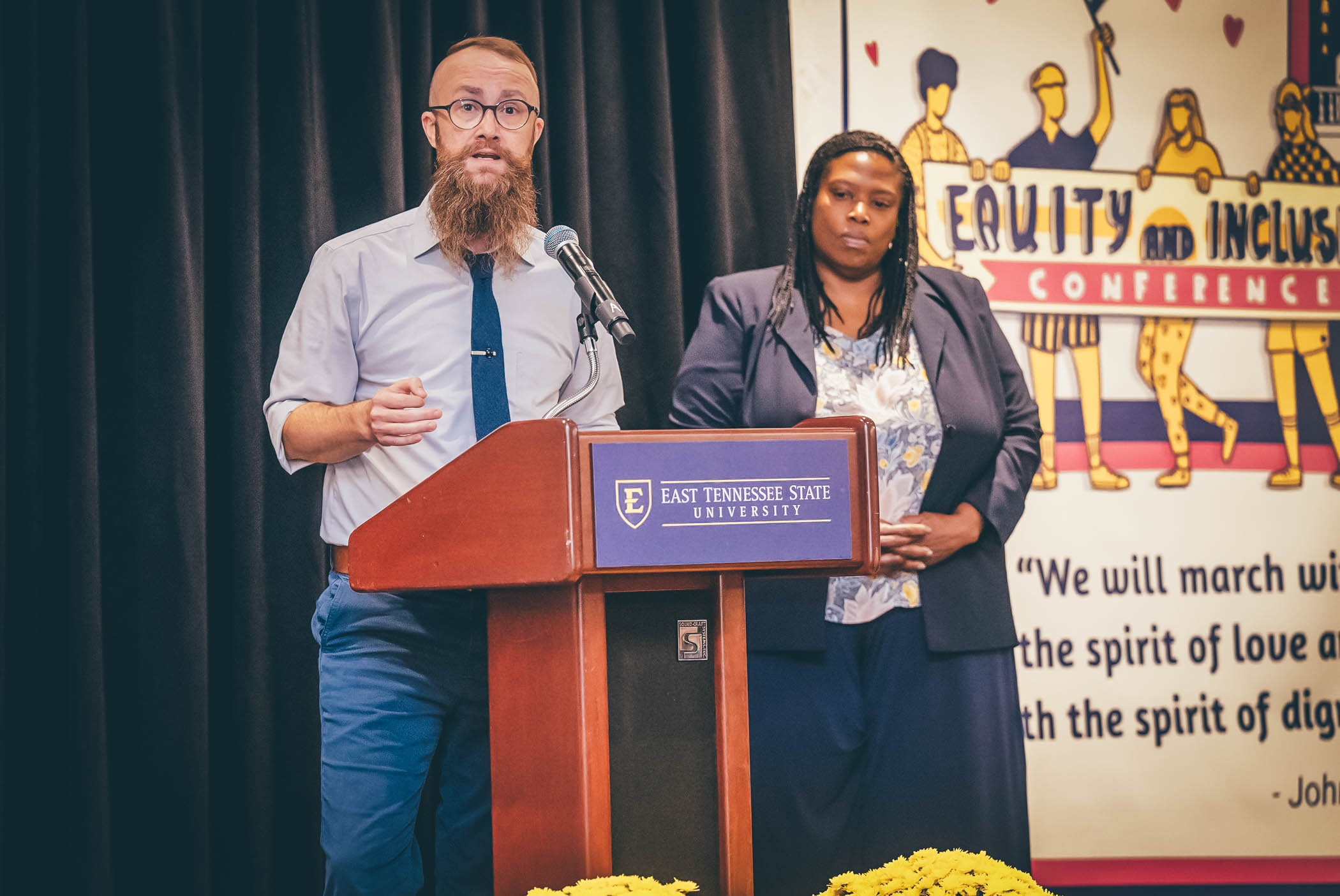 Conference co-chairs Ethan Hutchinson and Joy Fulkerson speak at the podium.