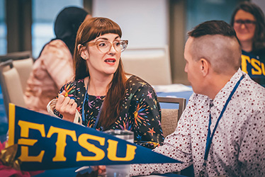 Conference attendees discussing at a table with an ETSU flag. 