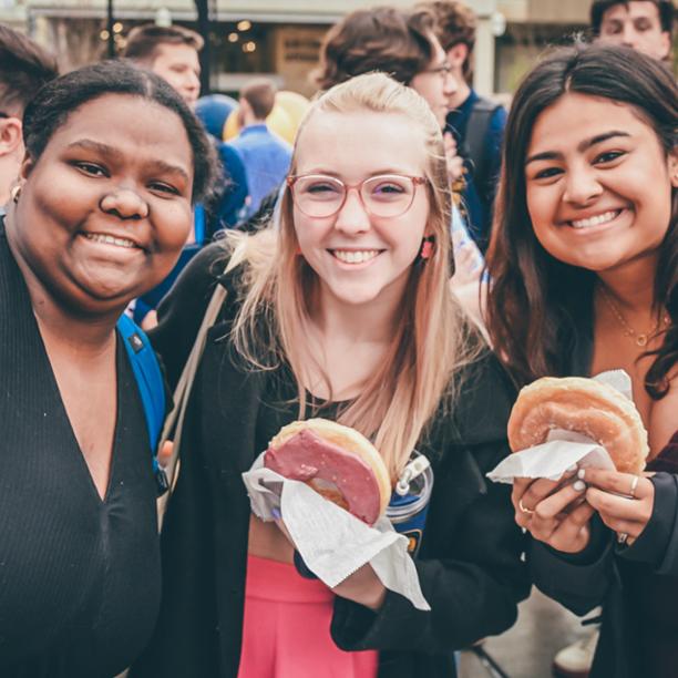 Three friends smile while enjoying doughnuts