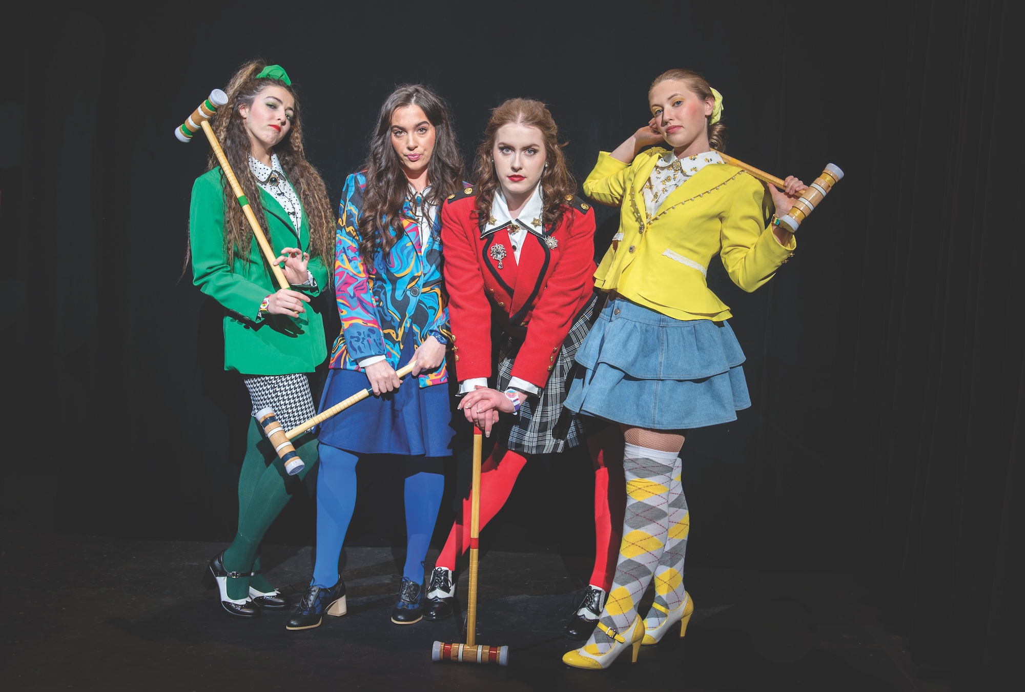 Group photo of four students posing in green, blue, red, and yellow blazers and skirts