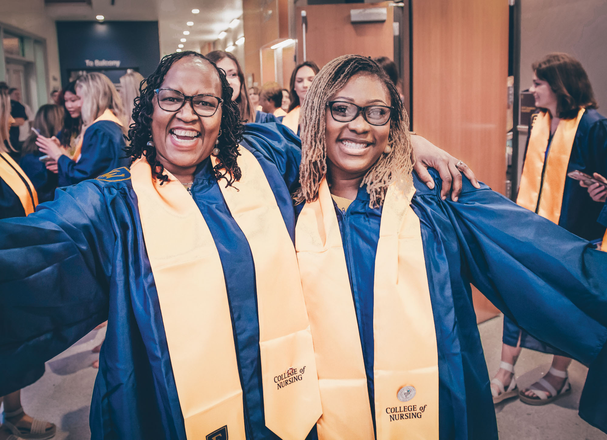 Two nursing students pose happily with their arms extended.