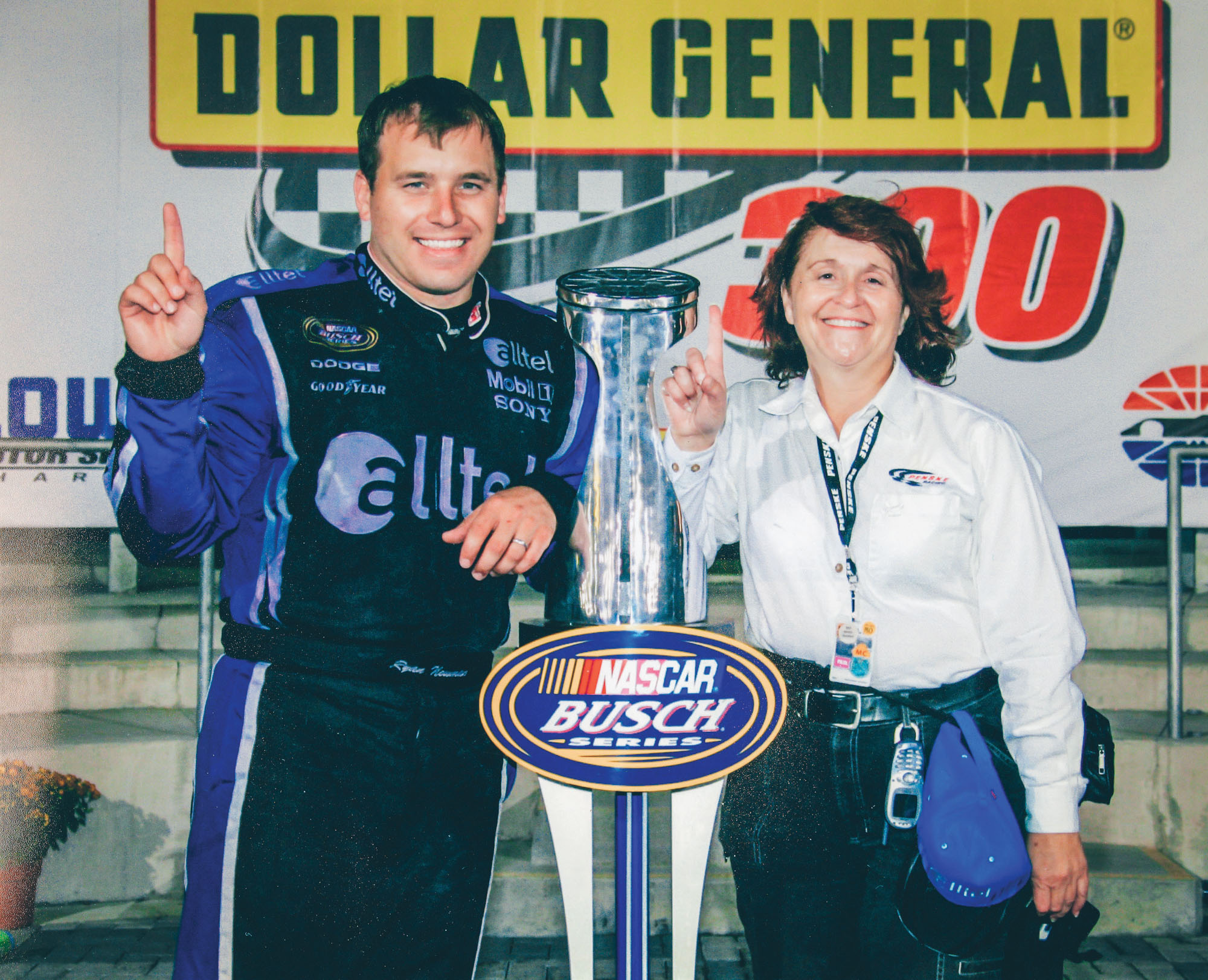 Deb Williams posing with a professional motorist with their pointer fingers raised in the air.