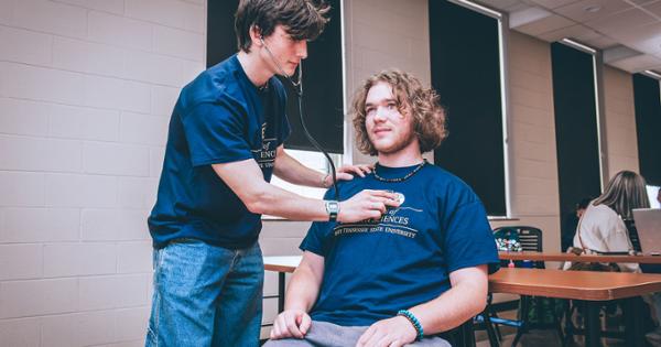 Student practicing with a stethoscope on another student