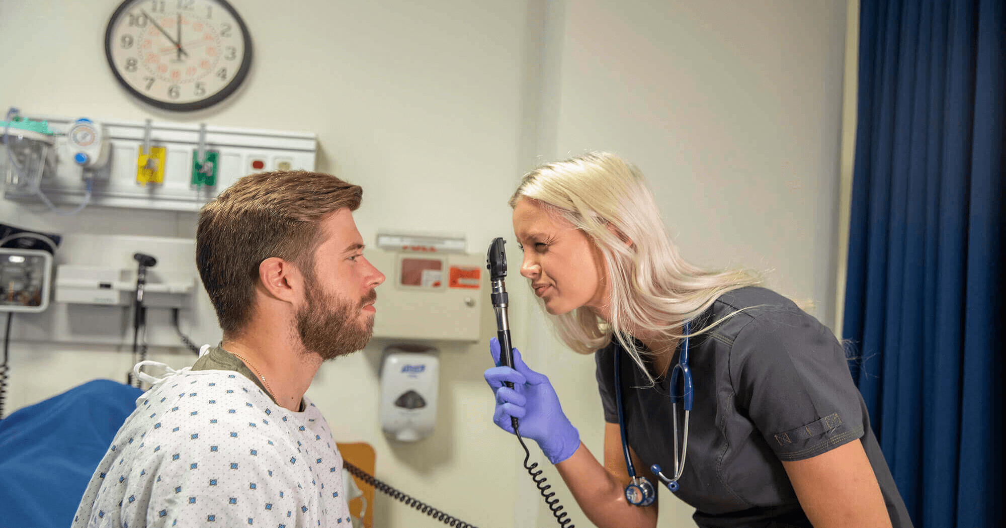 A nursing student checks the eyes of a young man.